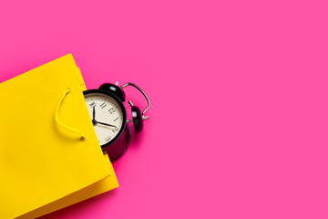 cool black alarm clock in beautiful yellow shopping bag on the wonderful pink background