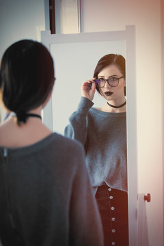 beautiful young woman standing in front of mirror and looking at her reflection