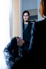 beautiful young woman standing in front of mirror, choosing what to wear and looking at her reflection