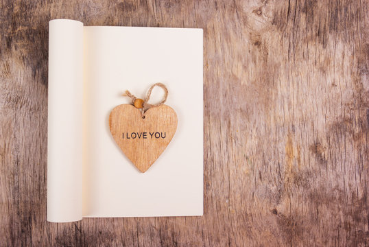Wooden heart on the background of an open diary with a blank page. Heart and notebook on a wooden background. Copy space.