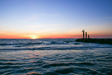 paysage au coucher de soleil sur la mer avec une digue et trois structures au bout dont une guérite