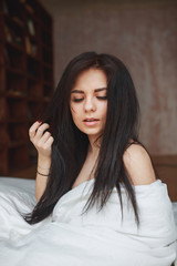 Sensual woman with dark hair sitting on a bed at home