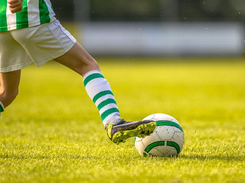 Boy kicking ball while playing soccer sport on natural grass pitch