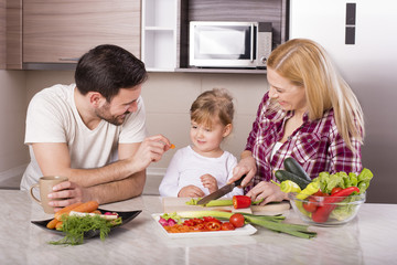 Young couple with kid having fun in kitchen while preparing fresh vegetable salad