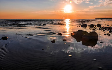 Fototapeta na wymiar Stones in water, waves on sandy beach of Gulf of Finland and wonderful sunset