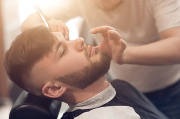 Obraz na płótnie Canvas a master in the barbershop works with the client. shaves beard young guy. shaving with a straight razor