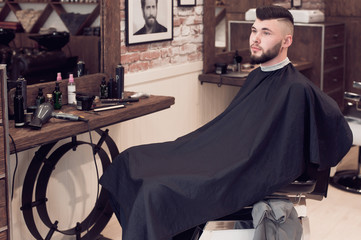 a young guy sitting on a chair in the barbershop. looking to the side - 138508228