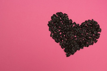 Heart laid out from sunflower seeds on a pink background.