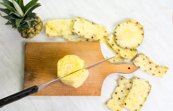Knife cutting pineapple on wooden board