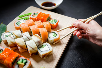 Sushi rolls and sauce and hand with chopsticks on a black background. Traditional Japanese food. Top view. Flat lay