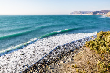 Turquoise rolling wave slamming on the rocks of the coastline