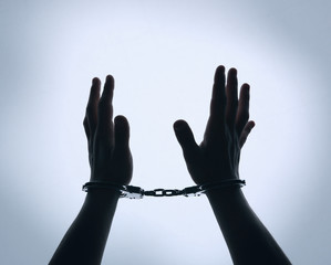 Black silhouette of man hands in handcuffs on light background