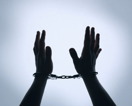 Black Silhouette Of Man Hands In Handcuffs On Light Background