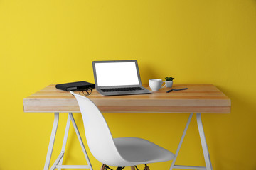 Workplace with laptop against yellow wall background