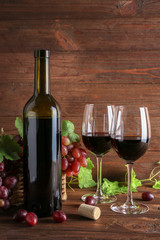 Wine bottle and glasses with grapes on wooden background