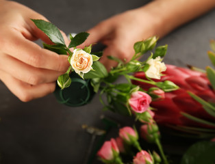 Female hands making beautiful bouquet of flowers on dark background