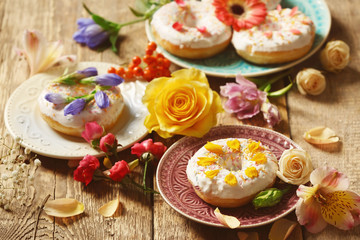 Obraz na płótnie Canvas Composition of plates with delicious donuts and colourful flowers on wooden table, closeup