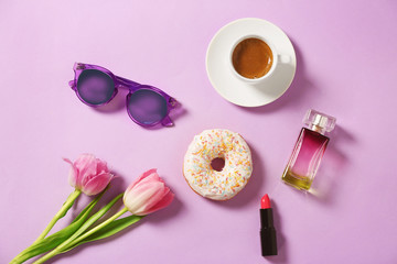 Obraz na płótnie Canvas Tasty doughnut, cup of coffee, flowers and cosmetics on violet background