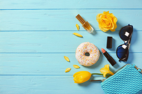 Tasty doughnut, flowers and cosmetics on blue wooden background