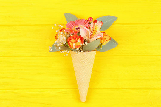 Waffle cone with composition of beautiful flowers on yellow background