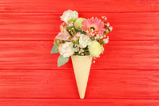 Waffle cone with composition of beautiful flowers on red background