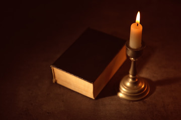 Bible and burning candle on table