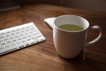 White Mug of Green Tea on a Wooden Office Computer Desk Table
