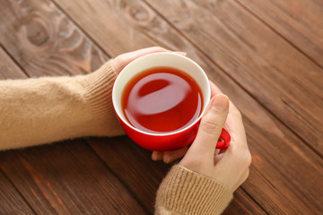 Female hands holding cup of aromatic tea on wooden background