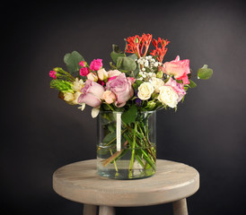 Glass vase with beautiful bouquet of fresh flowers on black background