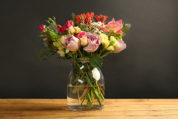 Glass vase with beautiful bouquet of  flowers on wooden table and black background