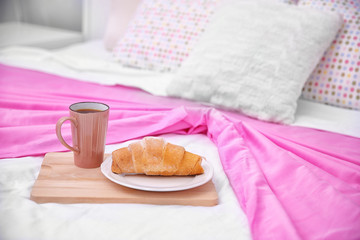 Cup of coffee and tasty croissant on bed