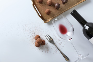 Delicious chocolate truffles and empty wine glass on white table