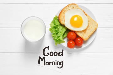Note with written phrase GOOD MORNING and tasty breakfast on table