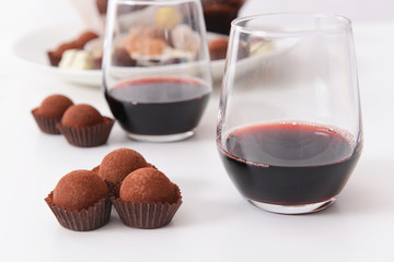 Delicious chocolate truffles and red wine on white background