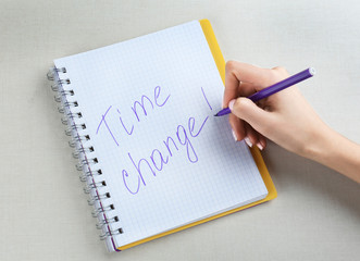 Female hand writing phrase TIME CHANGE in notebook