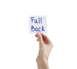 Female hand holding note with phrase FALL BACK on white background