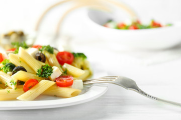 Pasta salad with tomatoes and olive on wooden table