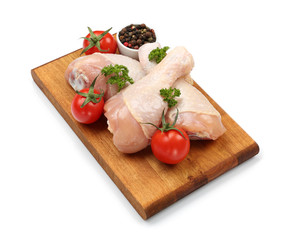 Wooden board with raw chicken legs on white background
