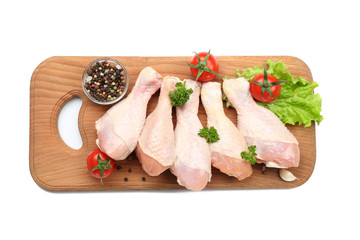 Wooden board with raw chicken legs on white background