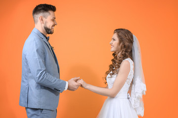 Happy wedding couple holding hands on color background