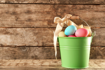 Metal bucket with colorful Easter eggs on wooden table