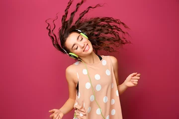 Fotobehang Beautiful young woman in headphones listening to music and dancing on color background © Africa Studio