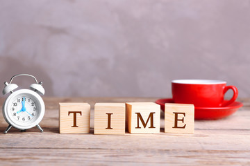 Cubes with alarm clock and cup on wooden table. Time concept