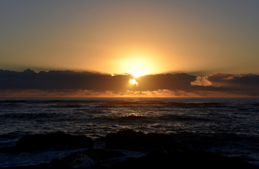 Beautiful sunrise cloudscape over ocean background. Sun rays beaming through picturesque clouds above sea. Blue sky with clouds, sea and sun on the horizon. Beautiful sunrise over the quiet calm sea.