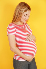 Young beautiful pregnant woman touching belly on yellow background