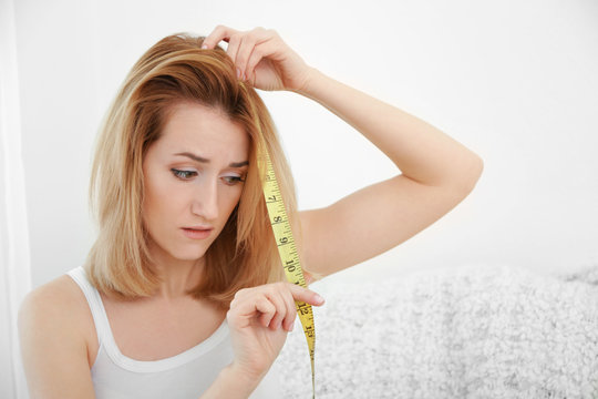 Beautiful young woman measuring length of hair at home