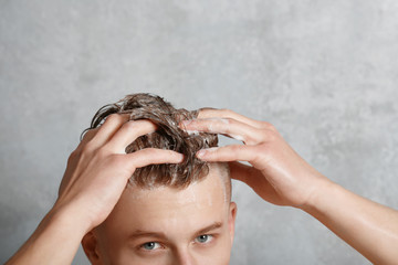 Young handsome man washing hair on gray background
