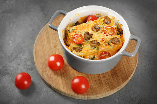 Delicious stuffed cannelloni with cherry tomatoes in ceramic pot on wooden board