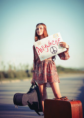 Beautiful young hippie girl hitchhiking on a road