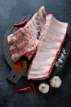 Dark wooden chopping board with raw seasoned pork ribs